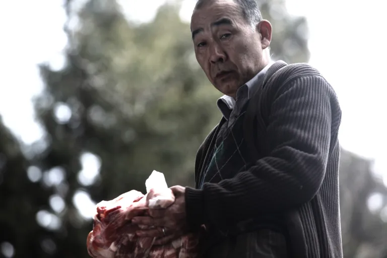 Yukio Murata nhìn xuống khi đang cầm một túi thịt đẫm máu